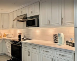 A modern kitchen with white cabinetry, a microwave, a toaster, and a coffee bar. - The St. Pete Beach Home (Saint Petersburg)