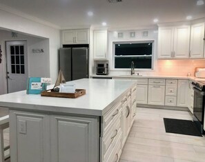 Una cocina moderna con armarios blancos, una isla grande, un refrigerador, un microondas y una ventana sobre el fregadero.