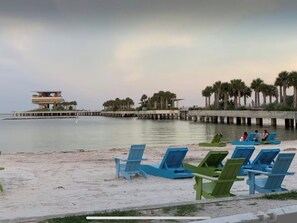 A beach with blue and green lounge chairs, a pier with buildings, and palm trees. - The St. Pete Beach Home (Saint Petersburg)