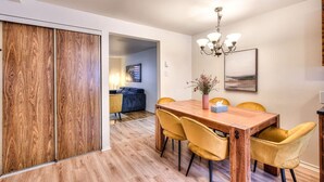 Un coin repas avec une table en bois et des chaises jaunes, un lustre et un tableau au mur.