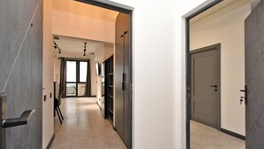 Een moderne hal met een neutraal kleurenpalet, een deur aan de rechterkant en zicht op een kamer met een groot raam.