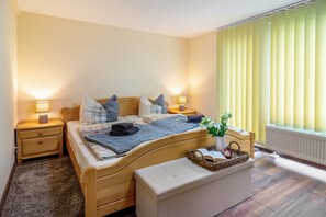 Een slaapkamer met een houten bed, nachtkastjes met lampen, een raam met jaloezieën en een radiator.