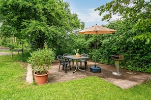 Een terras met een tafel en stoelen, omringd door groen en een hek.