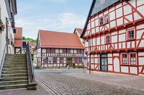 En brostensbelagt gade med traditionelle bindingsværkshuse, en trappe og en klar blå himmel.