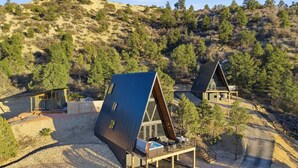 Eine moderne, hakenförmige Hütte mit einer Terrasse und Sitzgelegenheit im Freien, eingebettet in eine hügelige Naturlandschaft.