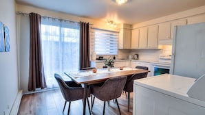 A modern kitchen with white cabinets, a dining table with chairs, and a built-in washing machine. - Montreal`s West Island Retreat! Value & Adventure! (Montréal)