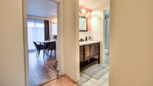 A hallway leading to a dining area with a table and chairs, a kitchen with a countertop and cabinets, and a bathroom with a toilet and sink. - Montreal`s West Island Retreat! Value & Adventure! (Montréal)
