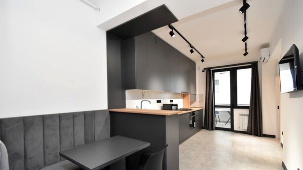 A modern kitchen with a built-in island, a dining area with a bench, and a TV mounted on the wall. - Cozy 1-bedroom apartment in adorable Yerevan with AC and Balcony (Yerevan)