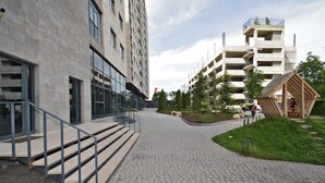 A modern building with a paved walkway, a wooden structure, and a landscaped area with trees. - Cozy 1-bedroom apartment in adorable Yerevan with AC and Balcony (Yerevan)