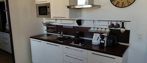 A modern kitchen with white cabinets, a stainless steel range hood, a microwave, a coffee maker, and a clock on the wall.