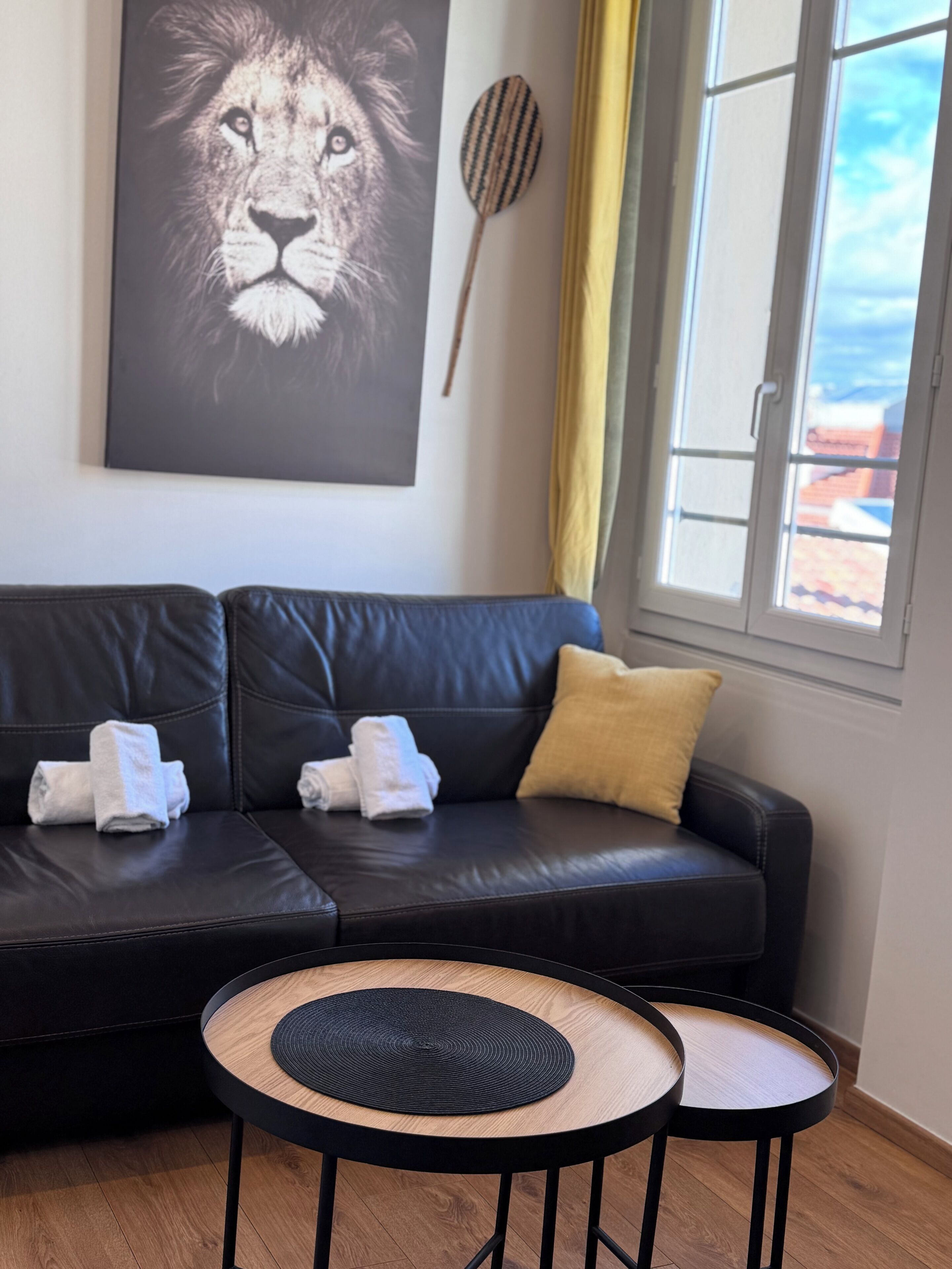 A black leather sofa with two towels, a wooden wall hanging, and a window with a view.