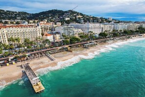 Eine Küstenstadt mit einem Hotel direkt am Strand, einer Pier und einer Promenade gesäumt von Palmen.