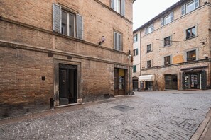 A cobblestone street with traditional brick buildings, a visible entrance to a building, and a small outdoor seating area. - La Corte Segreta - Urbino Historic Centre (Urbino)
