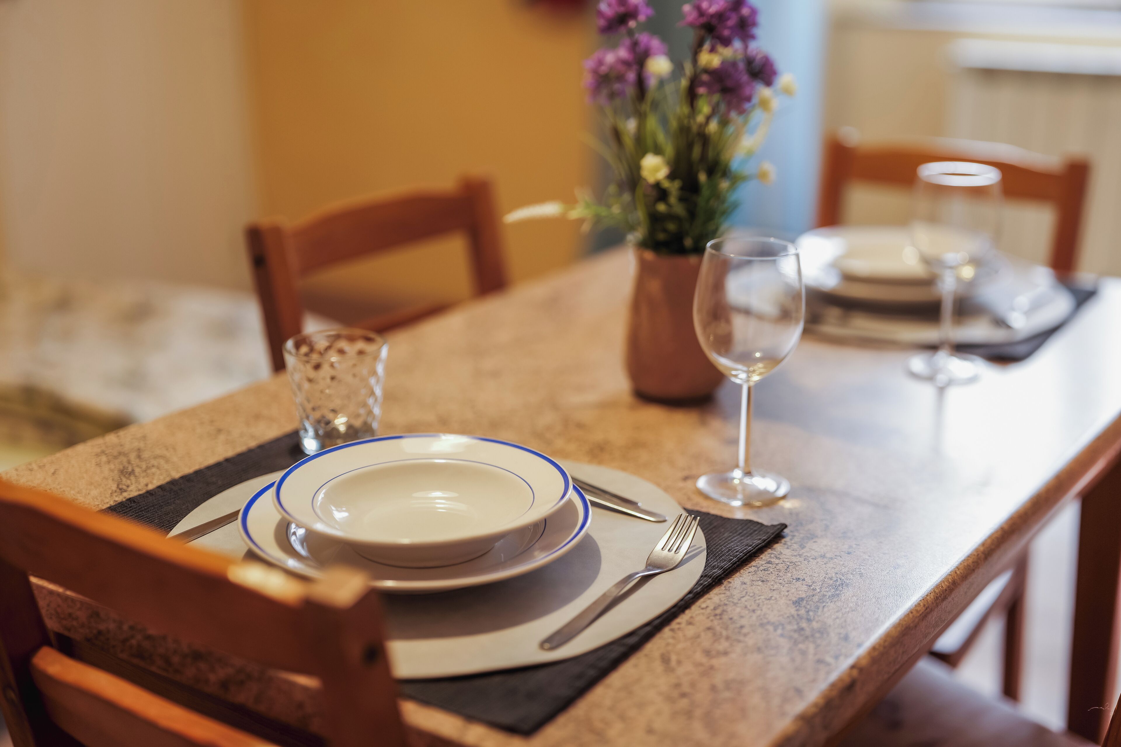 Une table à manger dressée avec des assiettes, des couverts et un verre.