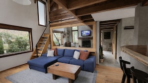 A modern living room with a blue sectional sofa, wooden coffee table, and a TV mounted on the wall.