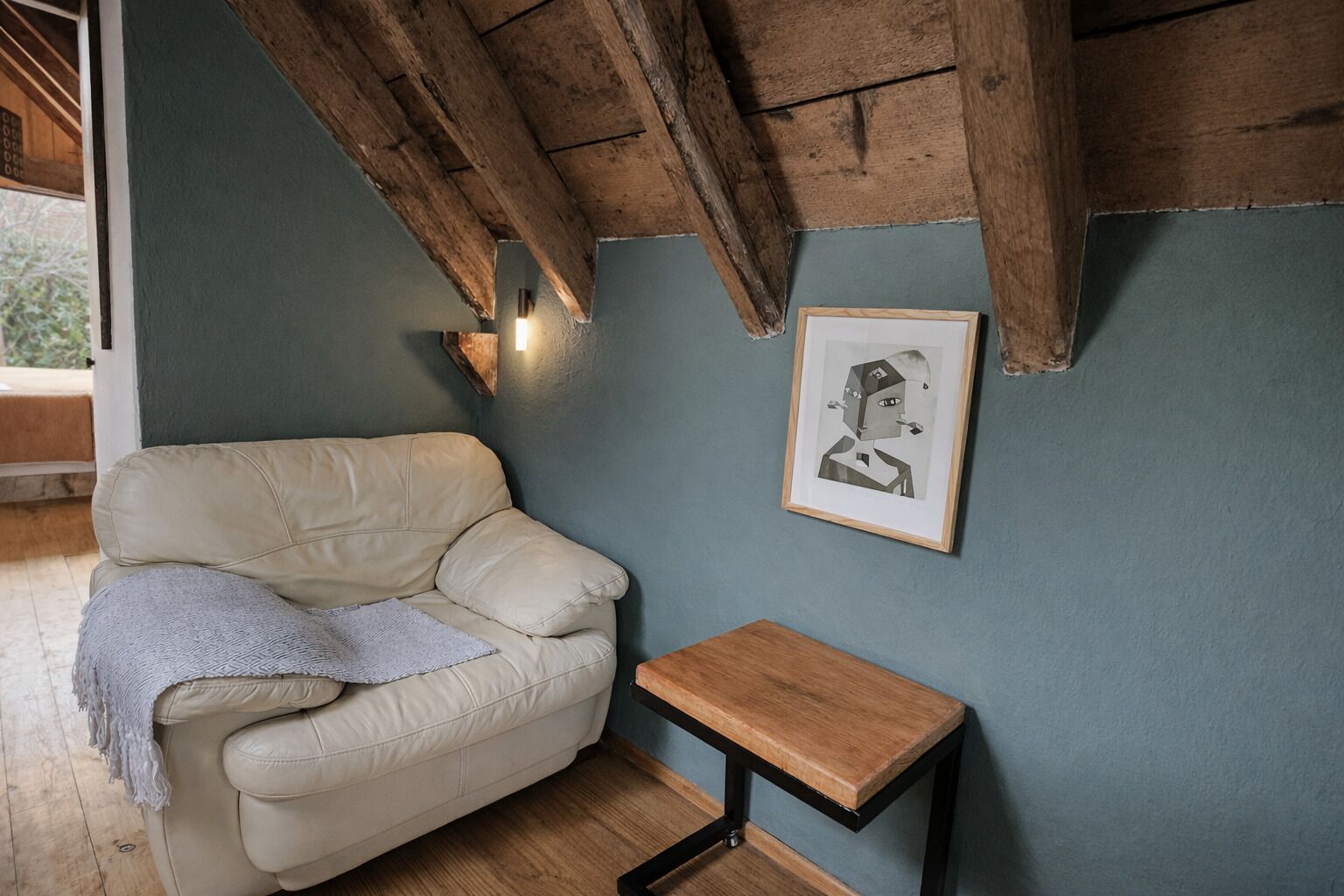 A cozy room with a leather armchair, a small wooden table, and a framed artwork on the wall.