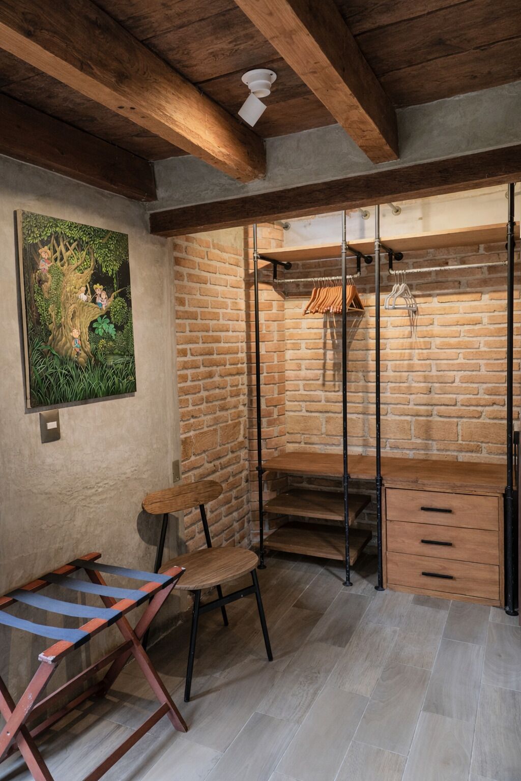 Quarto com paredes de tijolo aparente, teto de madeira e guarda-roupa em estrutura metálica com espaço para pendurar roupas.