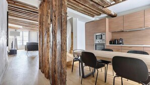 A modern kitchen with wooden cabinets, a dining area with a long table and chairs, and exposed wooden beams on the ceiling. - PARISIAN ELEGANCEWITH EXPOSED BEAMS PERFECTLY LOCATED-SAINT GERMAIN– RUE DU BUCI (Paris)
