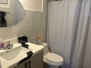 Une salle de bain avec un lavabo blanc, un miroir, des toilettes et un rideau de douche.