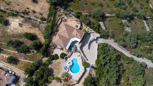 Vue aérienne d’une propriété comprenant une piscine, un espace patio et une grande maison avec un toit en tuiles.