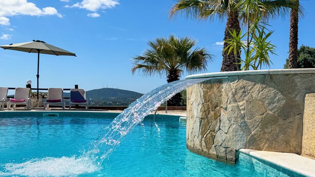 A pool with a water feature, lounge chairs, and palm trees.