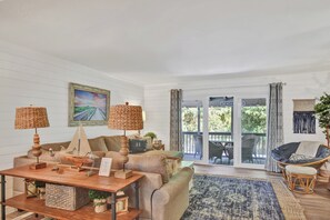 A cozy living room with a wooden coffee table, two lamps, a sofa, and a chair. There is a large window with a view of the outdoors. - 4 bedroom - 4.5 bath condo.  With Ocean views. (Saint Simons Island)