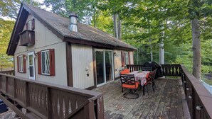 Una cabaña de madera con terraza, puerta corrediza de vidrio y patio con mesa y sillas.