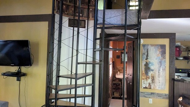 Una escalera de caracol con barandilla de metal, un televisor en la pared y un cuadro colgado.