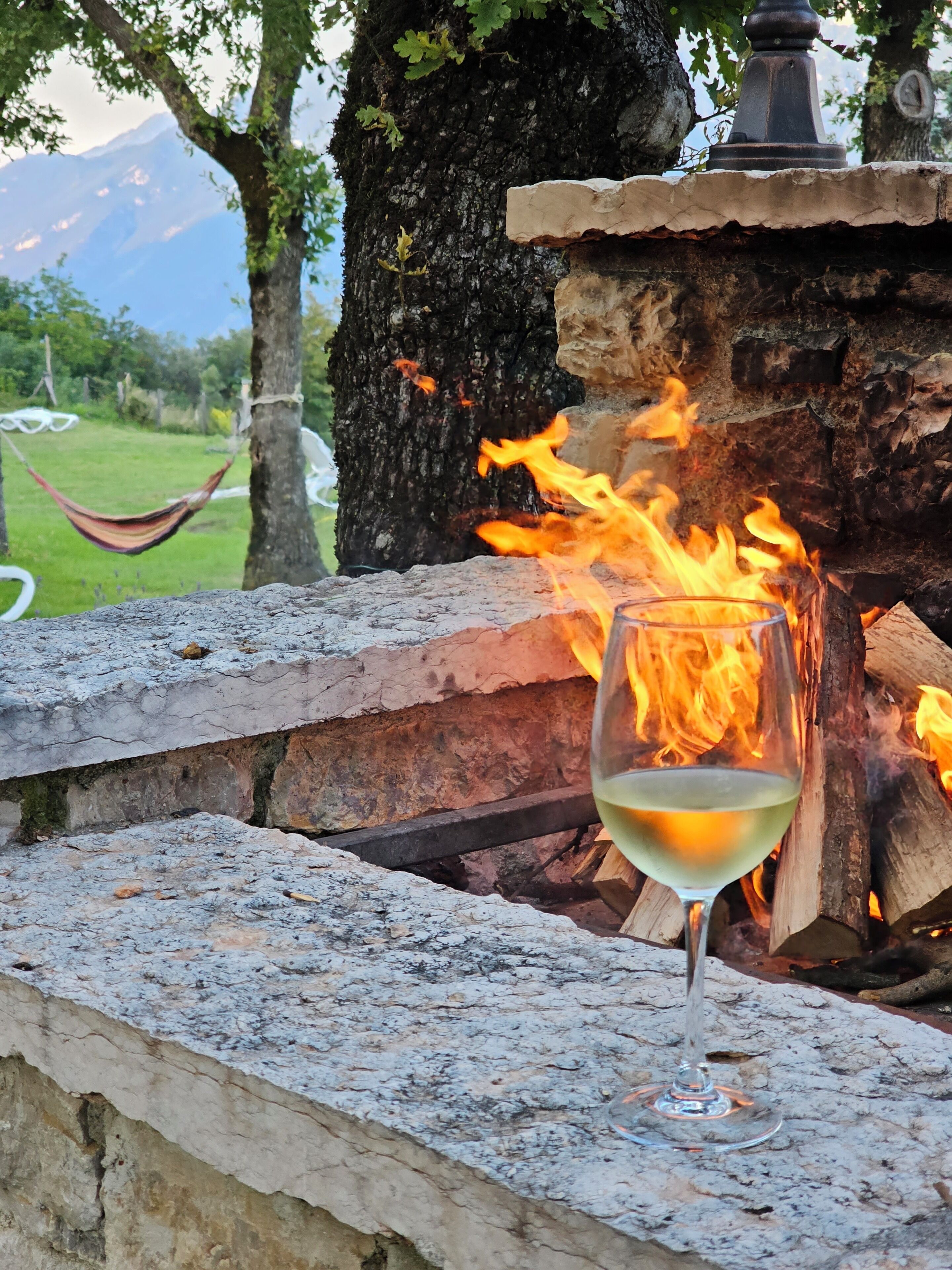 Una copa de vino blanco sobre un alféizar de piedra, con un fuego ardiendo al fondo.