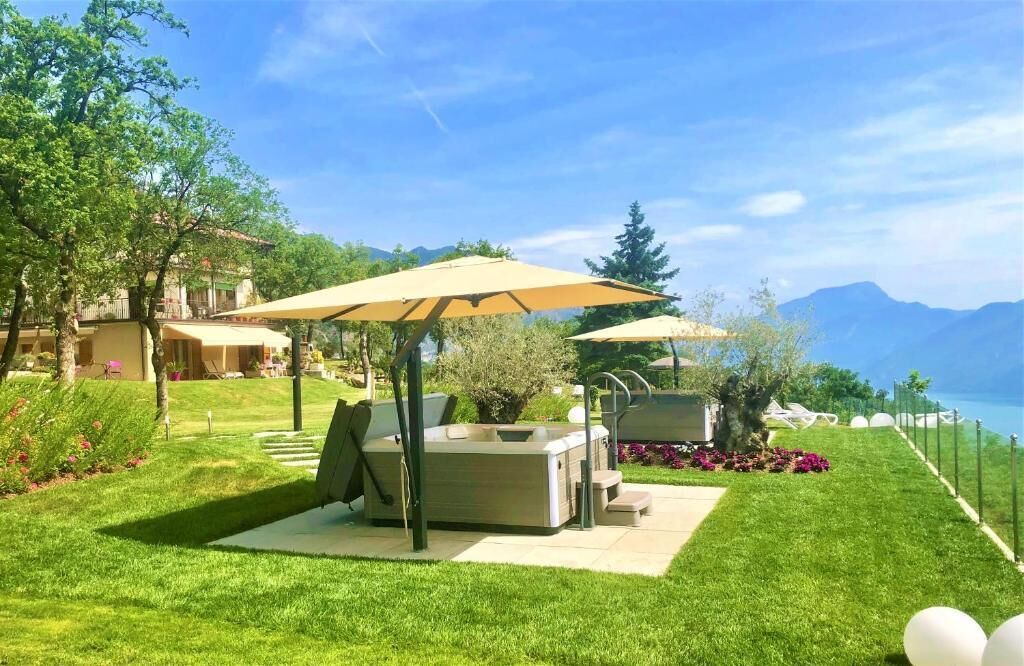 Un jardín cuidado con mobiliario exterior, bañera de hidromasaje y vistas panorámicas a las montañas y al lago.