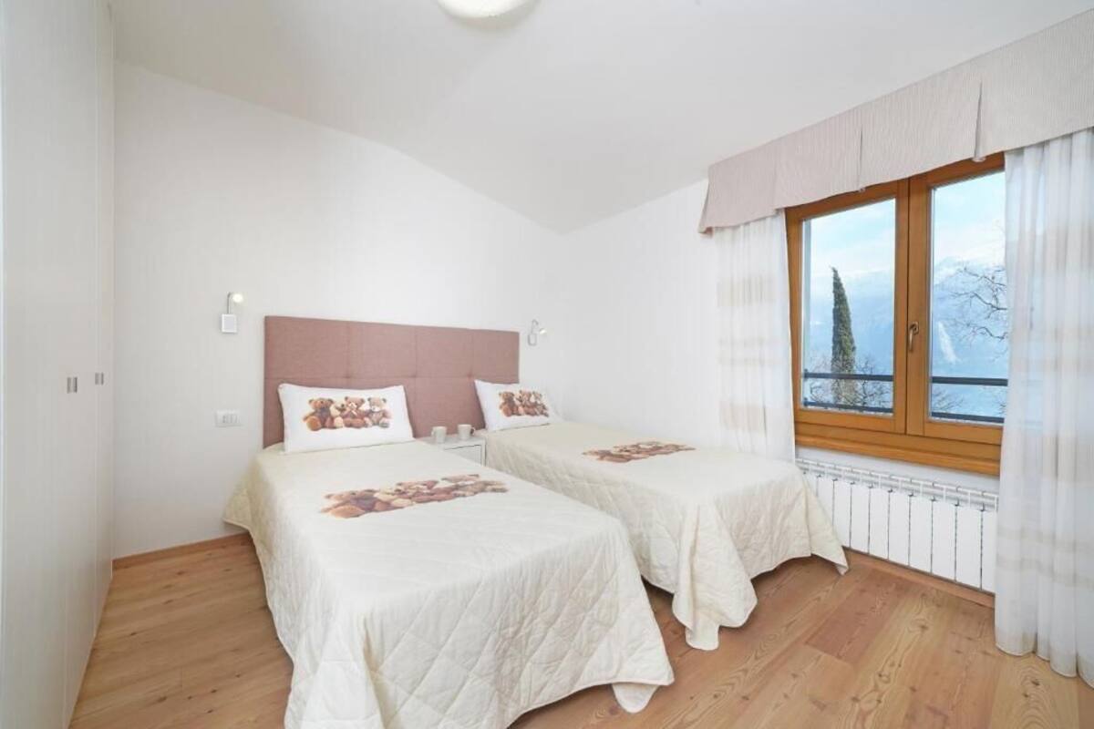 A bedroom with two beds, a wooden headboard, a window with curtains, and a view of trees.