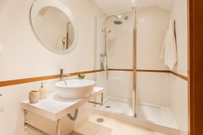 Un baño con un espejo redondo, un lavabo, una ducha y un perchero para toallas.
