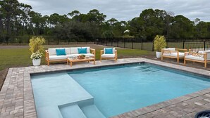 Un jardin avec une piscine, du mobilier d’extérieur et une zone délimitée par une clôture.