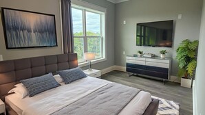 Une chambre moderne avec un grand lit, un téléviseur à écran plat, une commode et une fenêtre avec des rideaux.