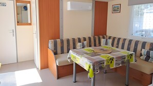 A compact living space with a sofa, a table, and a window. - Mobile Home '4 Personnes Climatisé À' with Shared Pool, Private Terrace and Air Conditioning (Saint-Pierre-d'Oléron)