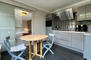 A modern kitchen with grey cabinets, a built-in oven, a microwave, and a coffee maker. There is a round wooden table with two chairs. - STUDIO FOR TWO PEOPLE (LE CROTOY)