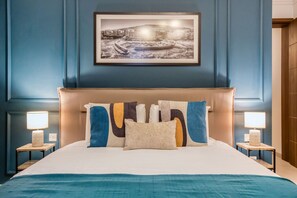Ein Schlafzimmer mit einem großen Bett, zwei Nachttischen inklusive Lampen, einem gerahmten Bild an der Wand und einer blauen Wand.