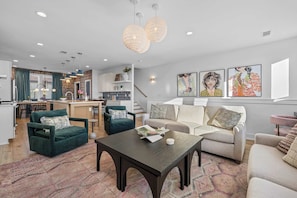 A modern living room with a dark wooden coffee table, a beige sofa, and a teal armchair. There is a kitchen in the background with a dining area. - Rooftop Hot Tub Views Parking Mins to Bway (Nashville)