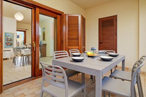 Un'area pranzo con tavolo apparecchiato per quattro, sedie, una porta e vista su un'altra stanza.