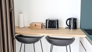 Eine kleine Küchenzeile mit einer Holzarbeitsplatte, einem Toaster, einem Wasserkocher und einem Papierhandtuchhalter.