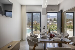 Et moderne spiseområde med et bord dækket til fire personer, store vinduer med udsigt til en pool og bjerge.