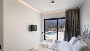 Et hotelværelse med seng, fjernsyn og udsigt til pool og bjerge.