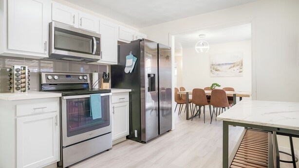 Een moderne keuken met witte kasten, roestvrijstalen apparatuur en een eethoek met een tafel en stoelen.