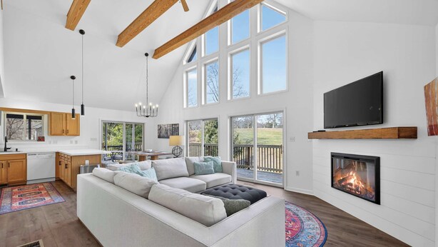 A spacious living room with a white sectional sofa, a fireplace, and a large TV mounted on the wall. - Game Room, FirePit, Screened Porch & Golf Views (Hedgesville)