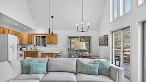 A modern kitchen with wooden cabinets, a white refrigerator, and a dining area with a table and chairs. - Game Room, FirePit, Screened Porch & Golf Views (Hedgesville)