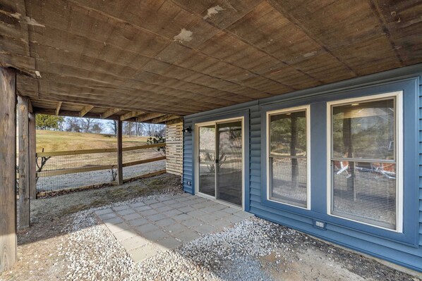 A covered patio area with a gravel floor and a wooden fence.