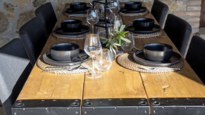 Een houten eettafel gedekt met zwarte kommen, wijnglazen en geweven placemats.