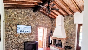 Een rustieke woonkamer met een stenen muur, een open haard, een televisie en een plafondventilator.