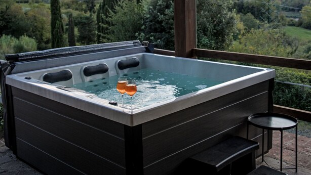 Een hottub met twee bierglazen, een houten terras en uitzicht op een vallei.