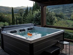 A hot tub with two glasses of beer, a wooden deck, and a view of a valley. - Nido di Falco by Interhome (La Sassa)